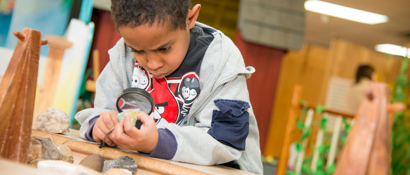 Child examining rocks under a magnifying glass.
